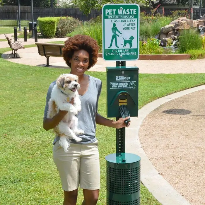 Commercial pet waste station with bag dispenser and lined trash bin beside a property walkway